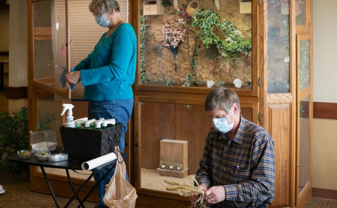 Mary Elgersma (left) cleans a window in a Pine Haven aviary while Mel removes old millet sprays from a wooden perch and replaces them with fresh millet, a food source.