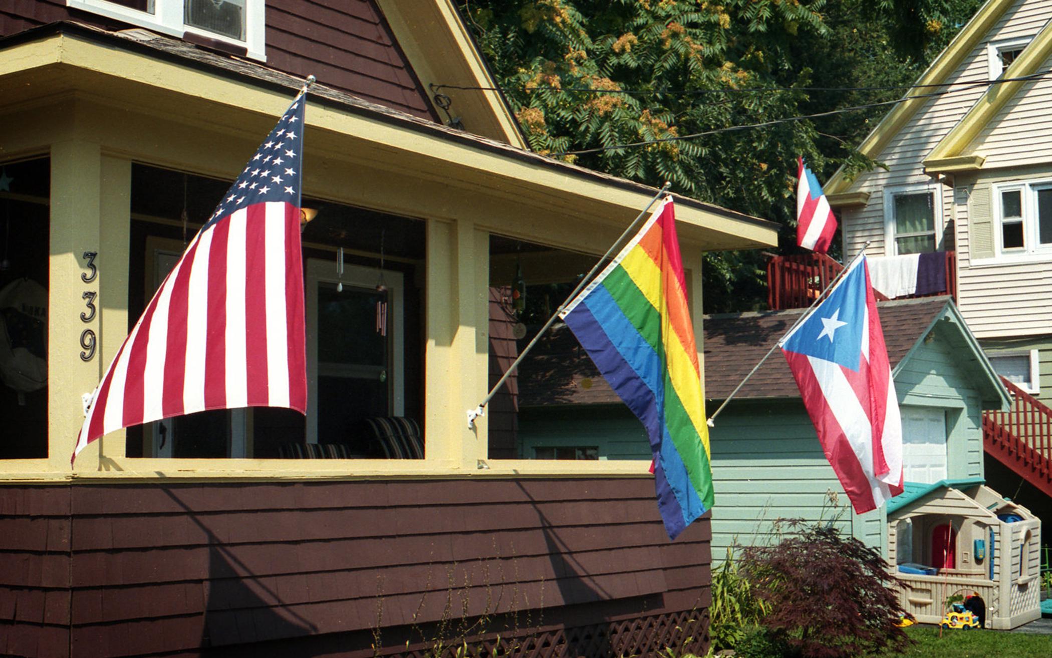 The author flies three flags on his front porch: the American flag, the Puerto Rican flag, and the Pride rainbow flag. He says the American flag honors his country and the other two flags honor his neighbors and friends.