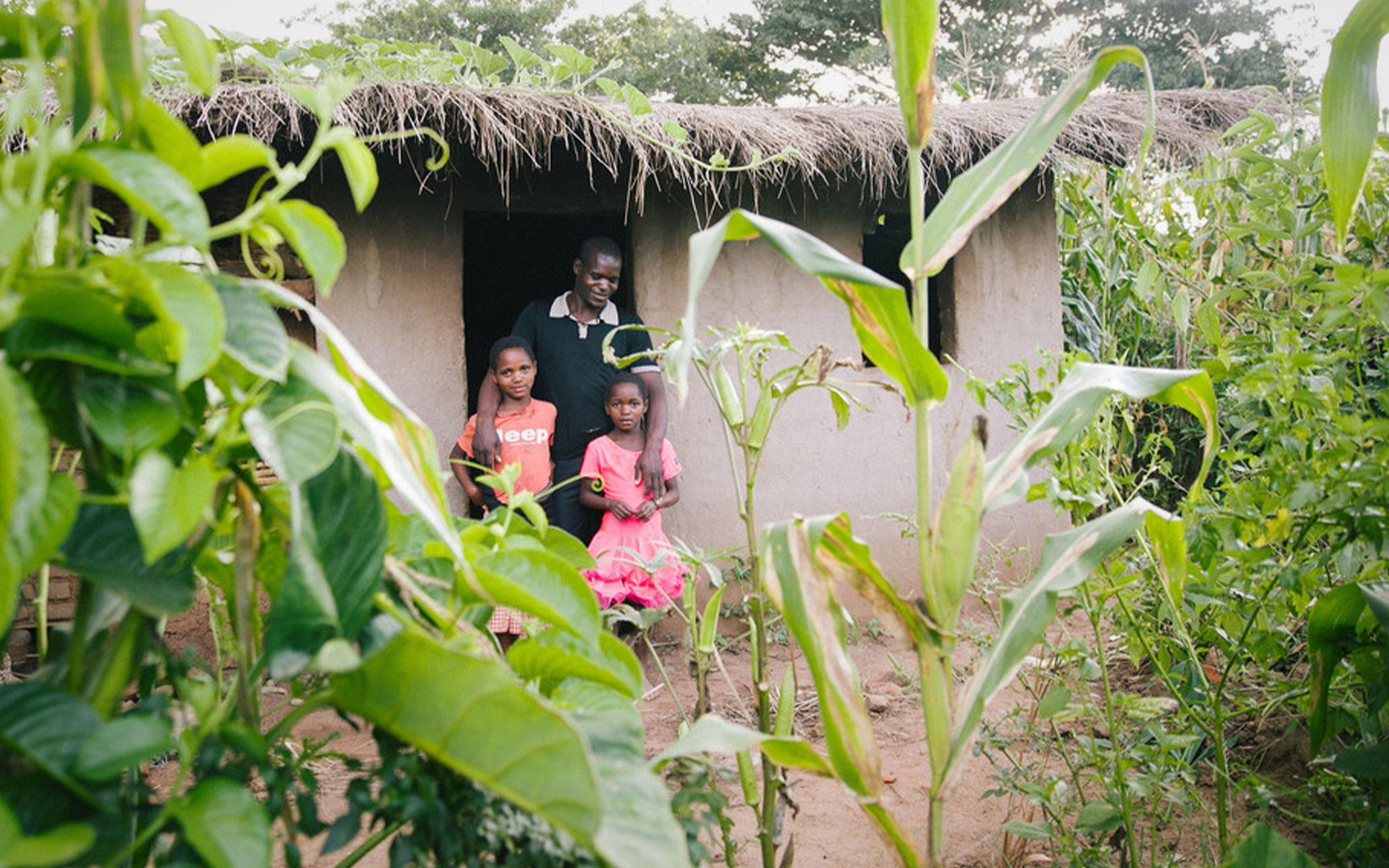 family in doorway of a grass-roofed house