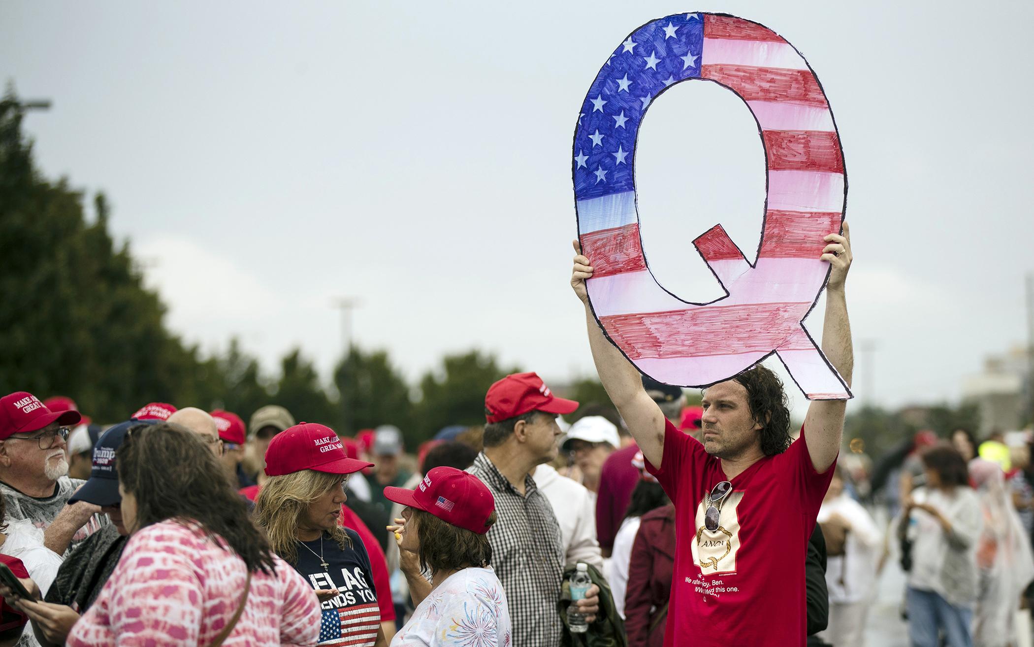 In this 2018 photo, David Reinert holding a Q sign waits in line with others to enter a campaign rally with President Donald Trump in Wilkes-Barre, Pa. 