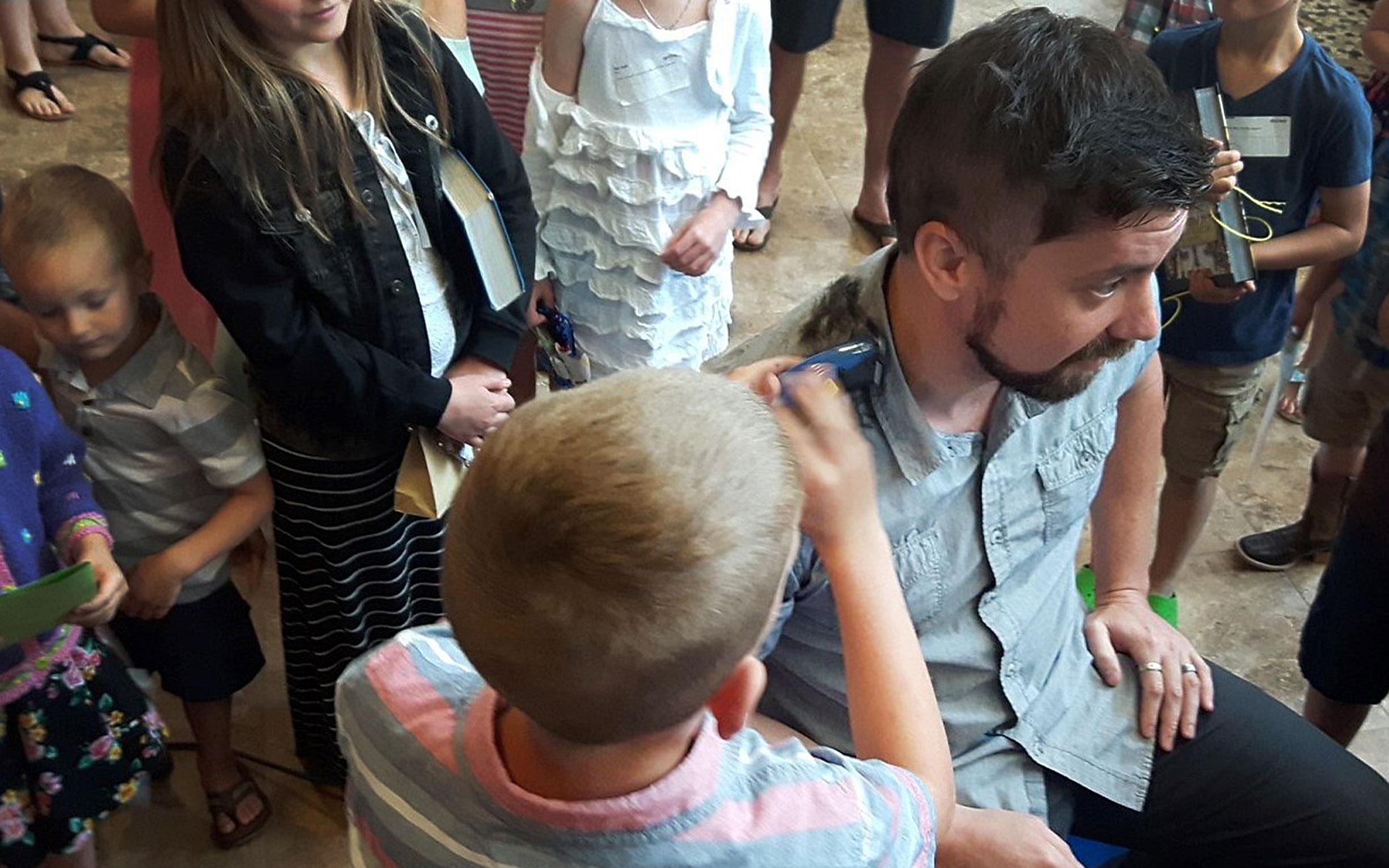 Children and young people watch as several take turns clipping pastor Justin Caruthers’ hair after a successful challenge. 